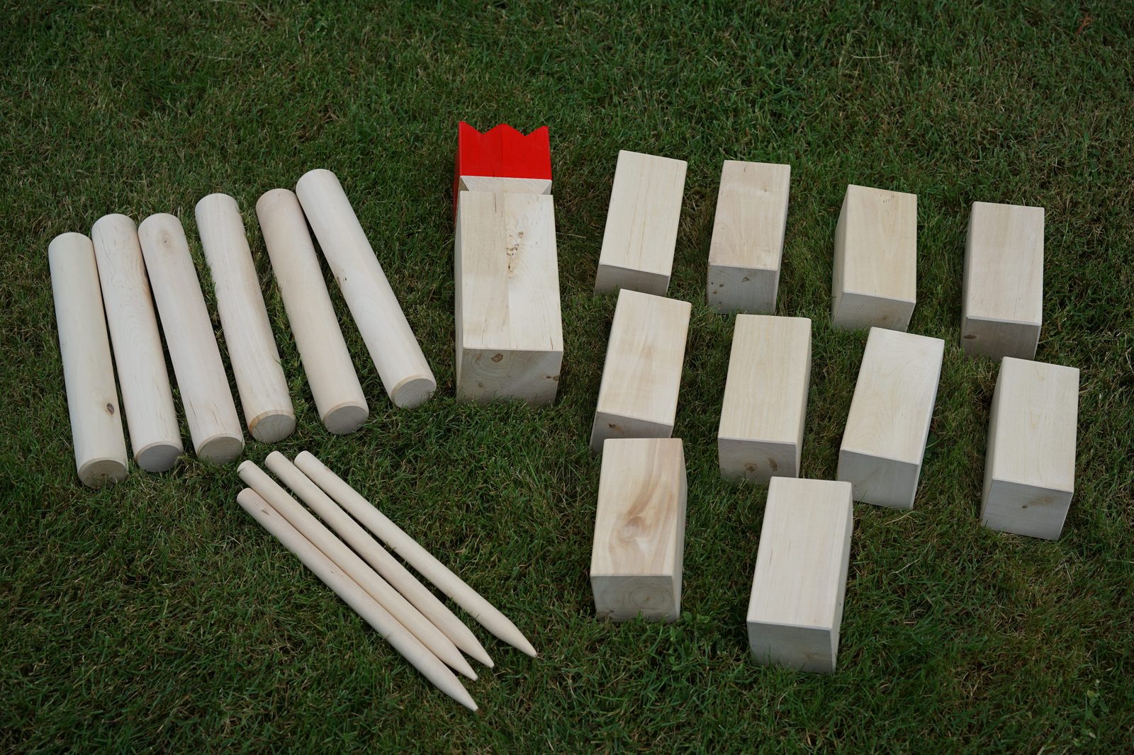 Kubb-Set: sechs Wurfhölzer, zehn Kubbs, König mit roter Krone und vier Eckstäbe auf einer Wiese